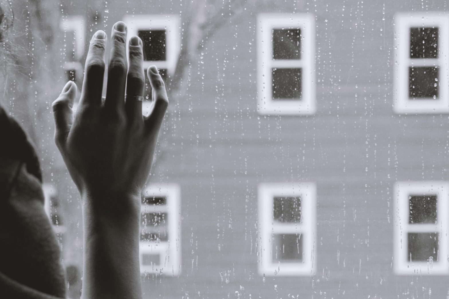 Photo by Kristina Tripkovic on Unsplash Black and white picture of a hand on a window and the window has drops of rain on it.