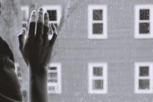 Photo by Kristina Tripkovic on Unsplash Black and white picture of a hand on a window and the window has drops of rain on it.