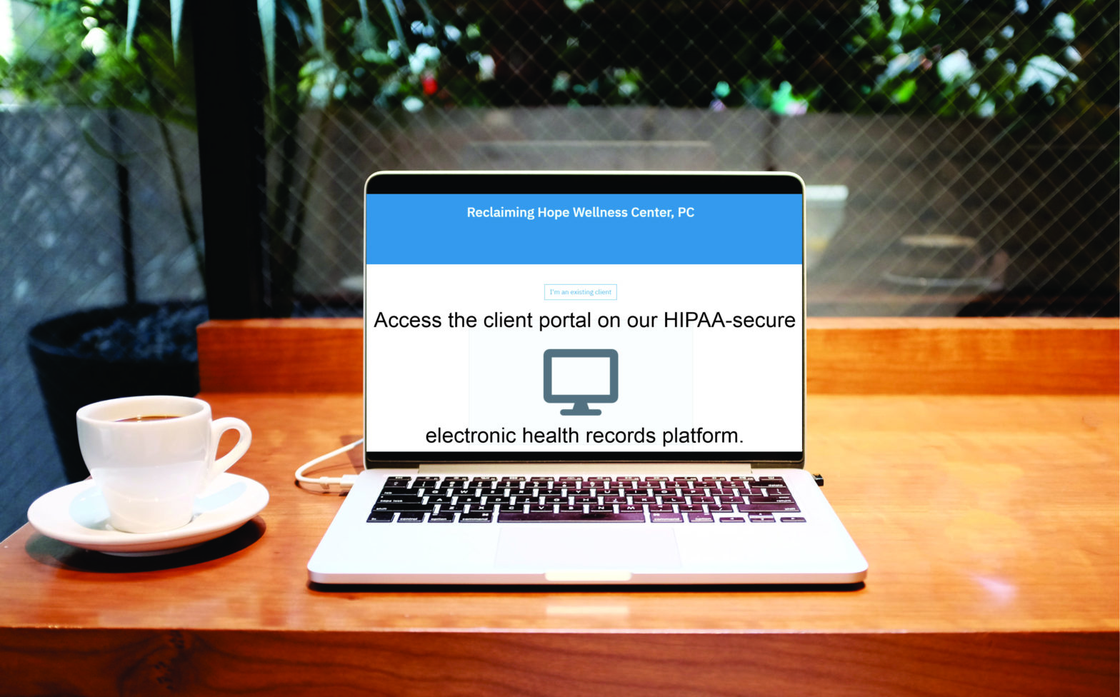 Picture of a laptop open to Reclaiming Hope Wellness Center's Client Portal. The laptop is sitting on a brown desk and there's a white mug and sauce sitting to the laptop's left on the desk. Photo of the computer on the desk by Alex Knight on Unsplash.